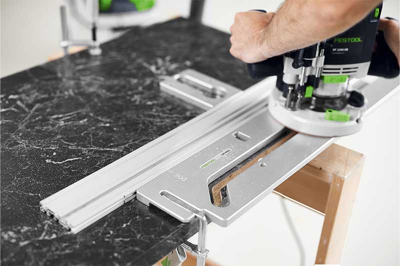 A tradesperson routes a workpiece with a routing template